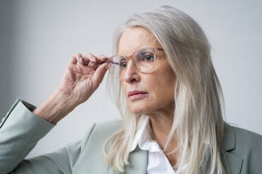 Worried businesswoman holding eyeglasses against white background - JOSEF08606