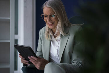 Happy businesswoman with tablet PC sitting on chair - JOSEF08619