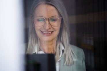 Smiling businesswoman with tablet PC seen through glass - JOSEF08625