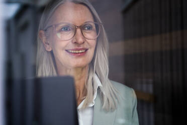 Thoughtful businesswoman with eyeglasses seen through glass - JOSEF08626