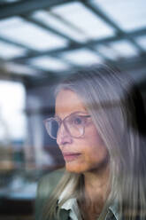 Senior businesswoman with eyeglasses looking through glass - JOSEF08627