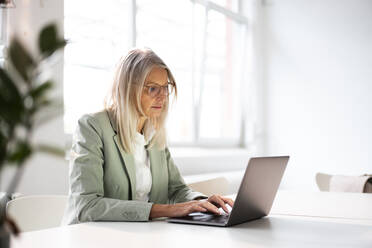 Senior businesswoman working on laptop at desk in office - JOSEF08634