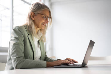 Lächelnde ältere Geschäftsfrau bei der Arbeit am Laptop im Büro - JOSEF08635