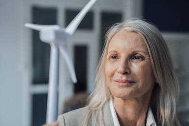 Businesswoman looking at wind turbine model at office - JOSEF08637