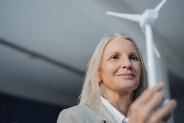 Senior businesswoman with wind turbine model at office - JOSEF08640