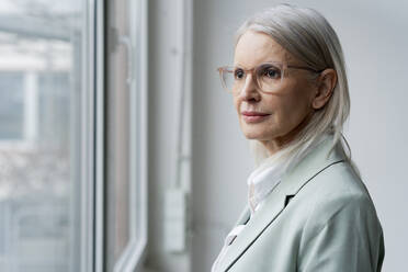 Contemplative businesswoman near window at office - JOSEF08648