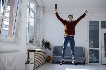 Happy businessman with tablet PC jumping in office - JOSEF08685