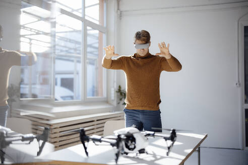 Geschäftsmann, der einen Virtual-Reality-Simulator trägt, gestikuliert am Schreibtisch im Büro - JOSEF08695