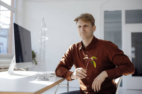 Nachdenklicher Ingenieur, der ein Blatt in der Hand hält und neben einem Modell eines Strommastes am Schreibtisch im Büro sitzt - JOSEF08715