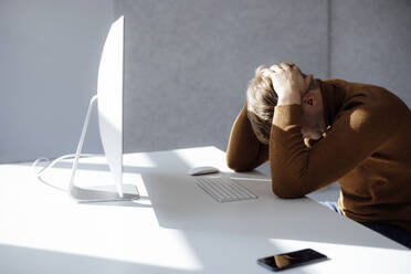 Businessman sitting with hands behind head at desk in office - JOSEF08729