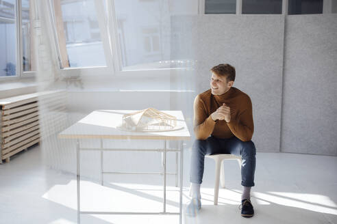 Glücklicher Architekt mit verschränkten Händen am Schreibtisch sitzend im Büro - JOSEF08738