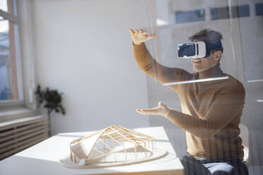 Smiling architect wearing virtual reality simulator gesturing sitting at desk in office - JOSEF08741