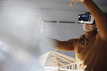 Businessman wearing virtual reality simulator gesturing in office - JOSEF08743