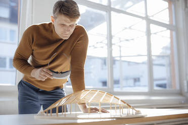 Businessman holding virtual reality simulator analyzing leaf shaped model in office - JOSEF08746