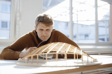 Architect examining leaf shaped model at desk in office - JOSEF08747