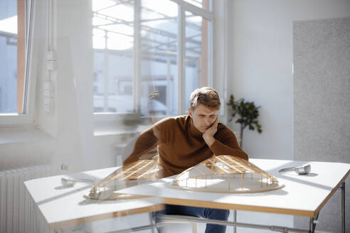 Architekt sitzt mit dem Kopf in der Hand und betrachtet ein blattförmiges Modell im Büro - JOSEF08752