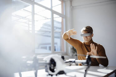 Businessman wearing virtual reality simulator gesturing at desk in office - JOSEF08754