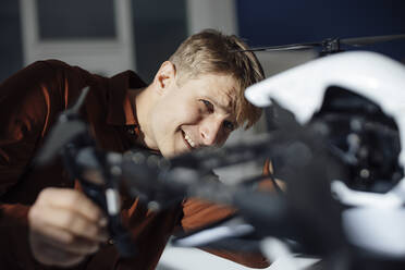 Smiling businessman examining drone in office - JOSEF08763