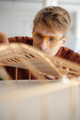 Architect wearing eyeglasses analyzing leaf shaped model at office - JOSEF08778