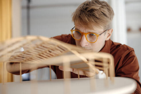 Architekt mit Brille, der ein blattförmiges Modell im Büro untersucht - JOSEF08779