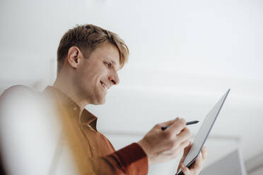 Lächelnder Geschäftsmann, der einen digitalisierten Stift hält und auf einen Tablet-PC im Büro schaut - JOSEF08782