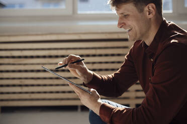 Zufriedener Geschäftsmann, der einen Tablet-PC mit digitalisiertem Stift im Büro benutzt - JOSEF08787