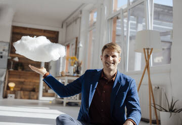 Happy businessman with levitating cloud network sitting in office - JOSEF08799