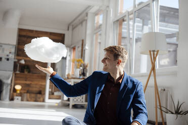 Happy businessman looking at levitating cloud network sitting in office - JOSEF08800