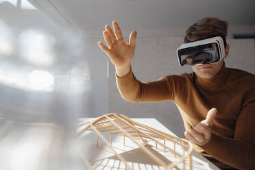 Architect wearing virtual reality simulator gesturing above leaf shaped model at desk in office - JOSEF08806