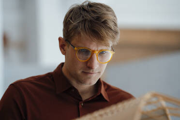 Businessman wearing eyeglasses examining leaf shaped model in office - JOSEF08831