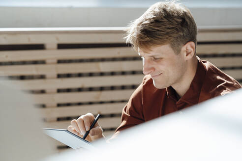 Lächelnder Geschäftsmann mit digitalisiertem Stift und Tablet-PC im Büro - JOSEF08839