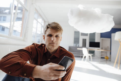 Geschäftsmann hält Smartphone sitzt durch schwebende Cloud-Netzwerk im Büro - JOSEF08853