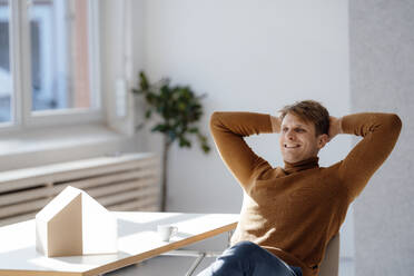 Lächelnder Architekt mit Händen hinter dem Kopf am Schreibtisch sitzend im Büro - JOSEF08878