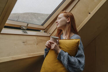 Junge Frau hält Kaffeetasse und schaut durch das Fenster - OGF01157