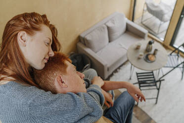 Young woman embracing boyfriend from back sitting in living room - OGF01160