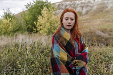 Young woman with blanket standing in field - OGF01197