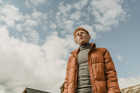 Contemplative teenage boy standing under cloudy sky - OGF01204