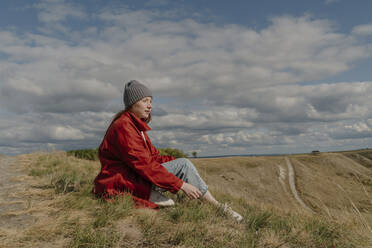 Junge Frau sitzt am Wochenende auf einem Feld - OGF01212