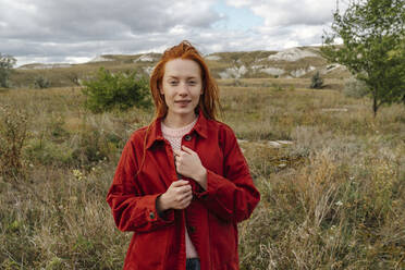 Redhead young woman standing in grass field - OGF01216