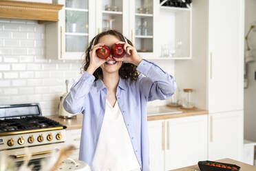 Lächelnde Frau, die ihre Augen mit Äpfeln in der Küche bedeckt - VPIF05839
