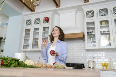 Happy woman juggling with apples in kitchen at home - VPIF05840