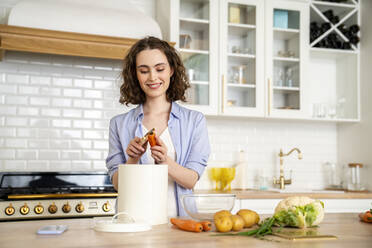 Lächelnde Frau schält Karotten am Esstisch in der Küche - VPIF05848