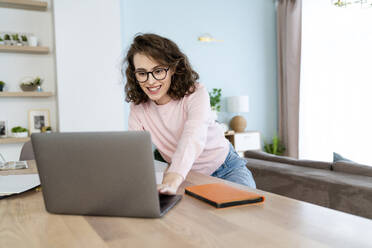 Happy student studying through laptop at table in living room - VPIF05884