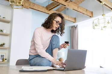 Studentin beim Online-Einkauf mit Kreditkarte über einen Laptop zu Hause - VPIF05893