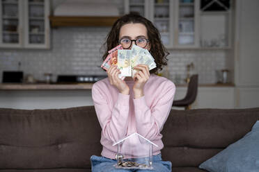 Junge Frau bedeckt den Mund mit Papierwährungen zu Hause - VPIF05900
