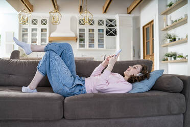 Woman using smart phone lying on sofa - VPIF05904