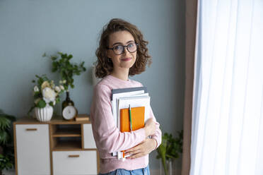 Lächelnde Studentin mit Buch im Wohnzimmer - VPIF05907