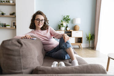 Lächelnde Frau sitzt zu Hause auf dem Sofa - VPIF05912