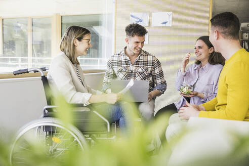 Junge Geschäftsleute bei einem Treffen im Büro mit einer Frau, die im Rollstuhl sitzt - UUF25706