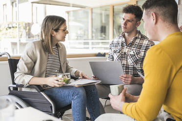 Junge Geschäftsleute bei einem Treffen im Büro mit einer Frau, die im Rollstuhl sitzt - UUF25708